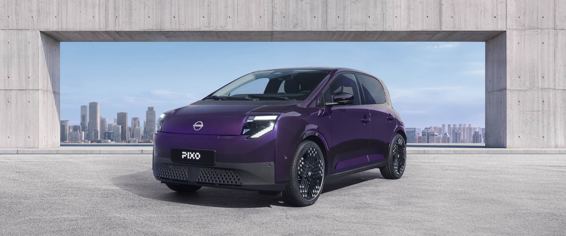 Three-quarter front view of a purple Nissan PIXO electric city car parked beneath a modern concrete structure, with a city skyline in the background.